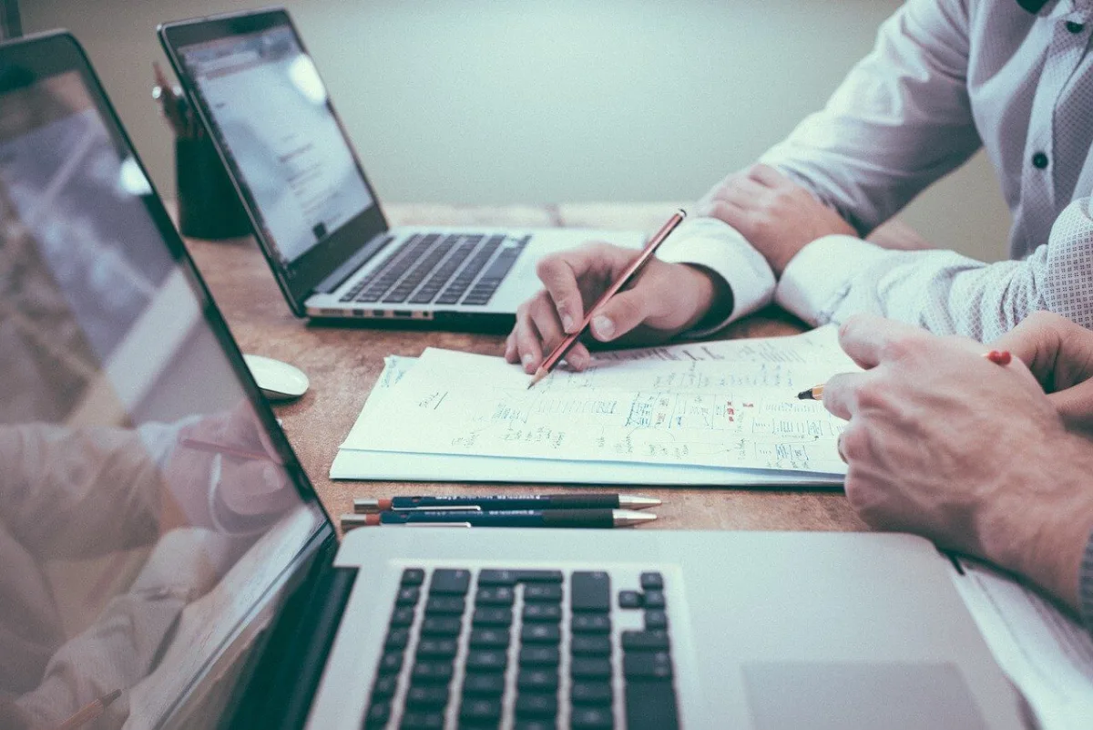 Dos personas revisando un plan de trabajo junto a varios portátiles